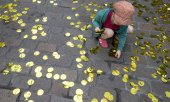 Ein Kind sammelt goldenes Konfetti der Schweizer Kampagne für das bedingungslose Grundeinkommen auf. (© picture-alliance/dpa)