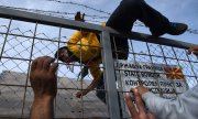 An Afghan refugee clambers over the fence at the border between Greece and Macedonia in Idomeni. (© picture-alliance/dpa)
