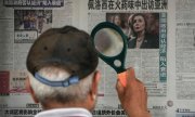 Mit einer Lupe schaut ein Zeitungsleser in Peking auf die Headline zur Pelosi-Reise. (© picture alliance / ASSOCIATED PRESS / Andy Wong)