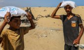 Young people carrying food bags handed out at a distribution centre in Rafah on 30 July. (© picture alliance / newscom / Anas Deeb)