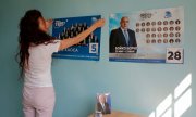 A woman hangs up a campaign poster for GERB, the party of former PM Borisov (© picture-alliance/Valentina Petrova)