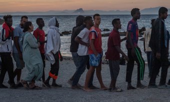滯留在休達的移民在食物發放點外的海灘上排隊。背景是西班牙大陸和直布羅陀岩。 （© 圖片聯盟／美聯社/安東尼奧森佩雷）