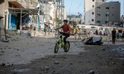 Gazze Şeridi'nde hasarlı binalar arasında bisiklete binen bir çocuk. (© picture-alliance/Khalil Hamra)