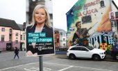 Batı Belfast'taki bir duvar resminin önünde bulunan seçim afişi. (© picture alliance / ASSOCIATED PRESS / Peter Morrison)