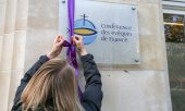 Eine Vertreterin des Opferverbandes "De la parole aux actes" befestigt eine lilafarbene Schleife am Eingang der französischen Bischofskonferenz. (© picture alliance/NurPhoto/Michel Stoupak)